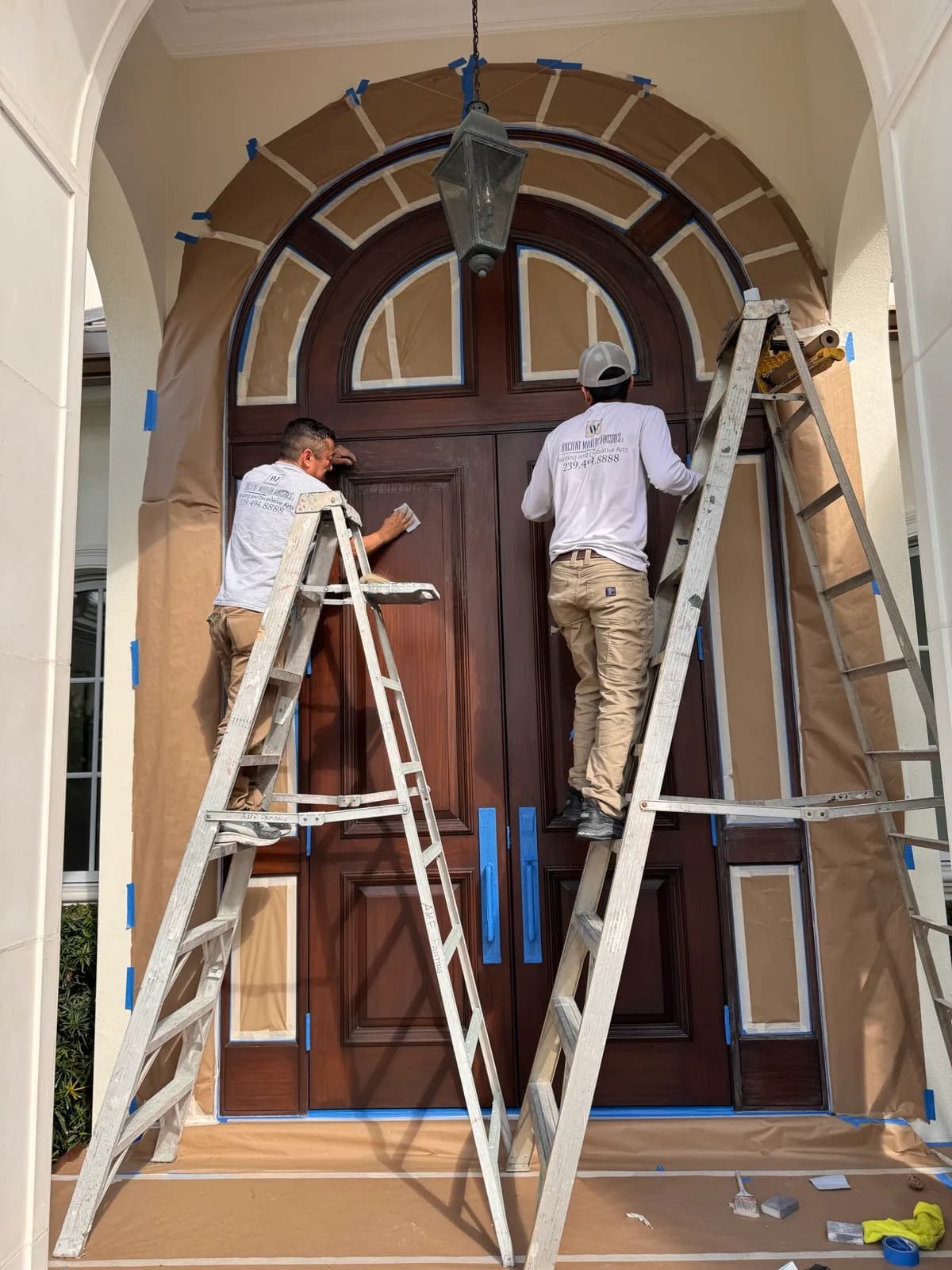 Two crew members working an arched entry door from ladders