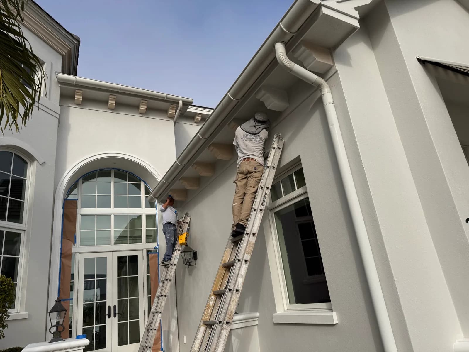 Crew member on a ladder working the eaves of a stucco home