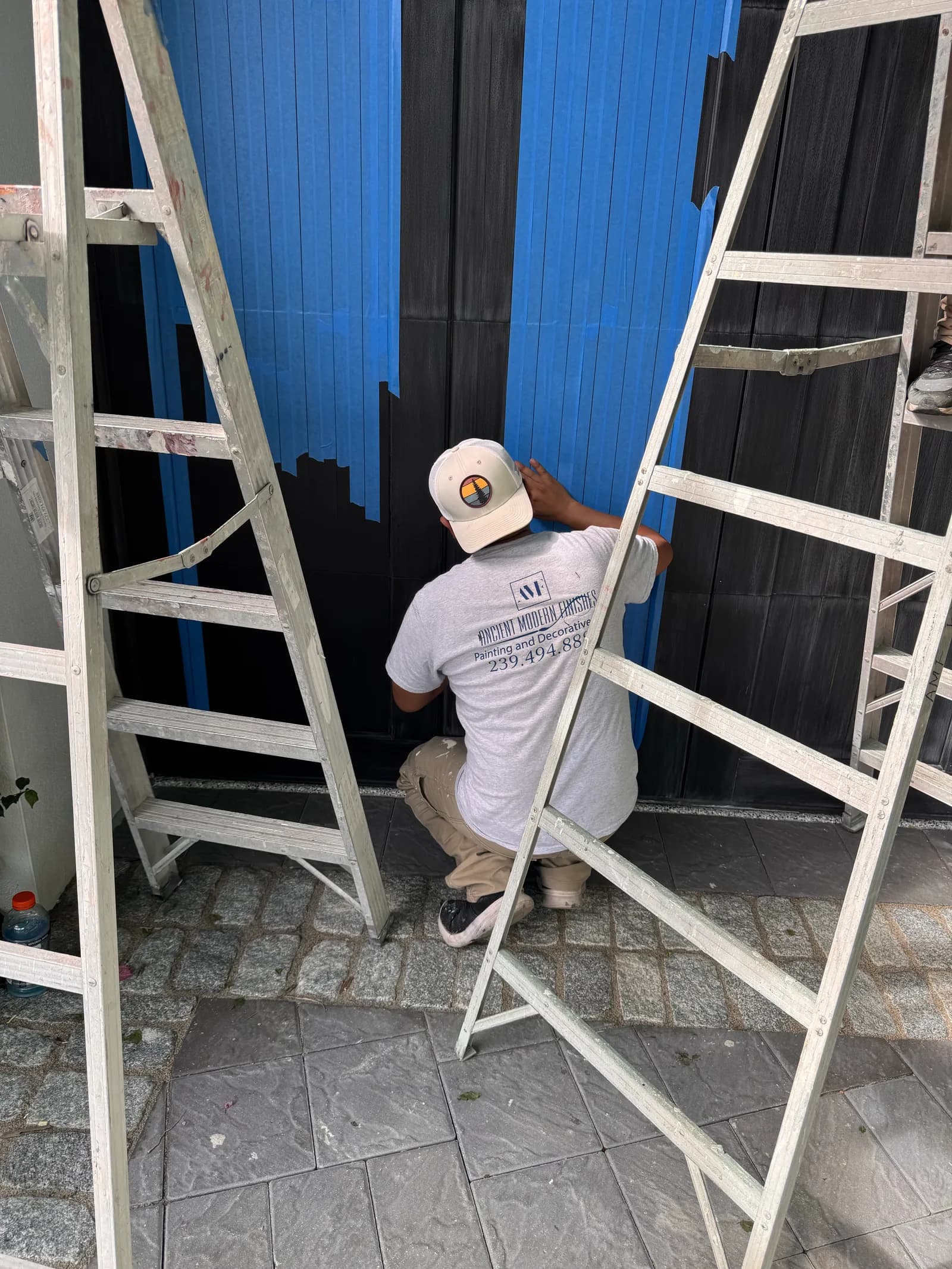 Crew member finishing a black garage door between two ladders